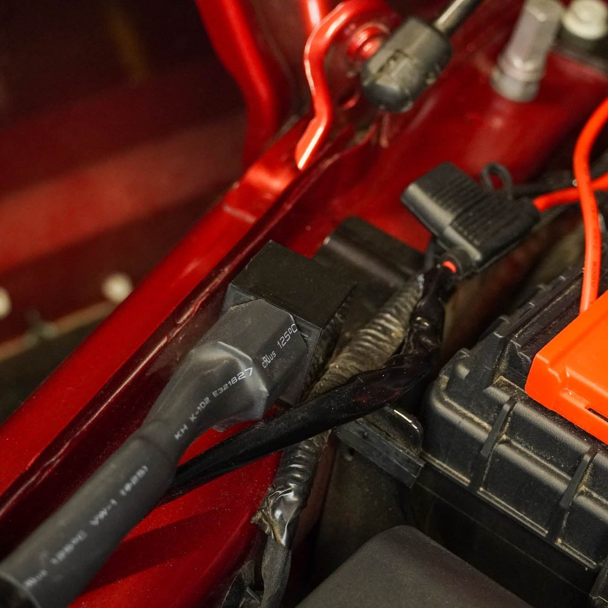 Close-up of a car battery with 40 Amp Wire Harness with DT Connector & Switch connected inside a vehicle.