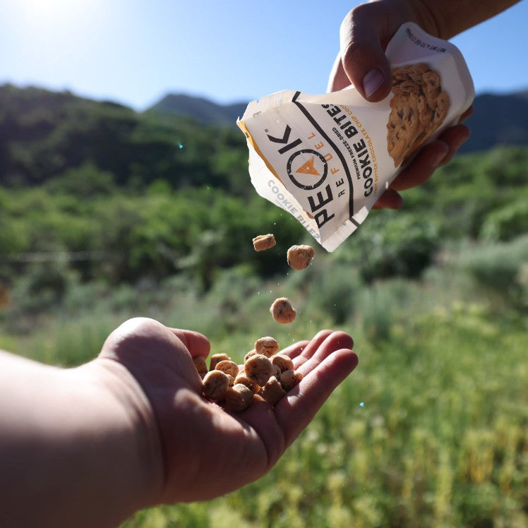 A hand pouring food out of a bag, holding a package of cookies, and small rocks.