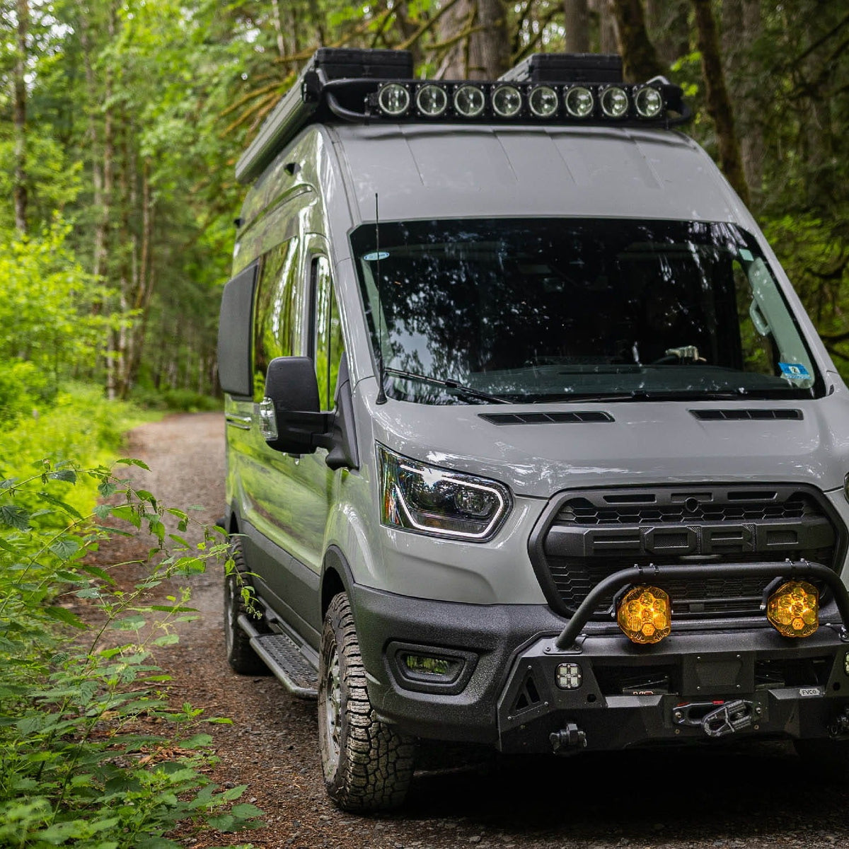 Front view of Ford Transit Van with FVC Transit Side Steps, Safari Roof Rack, and Core Front Bumper installed while driving through the woods
