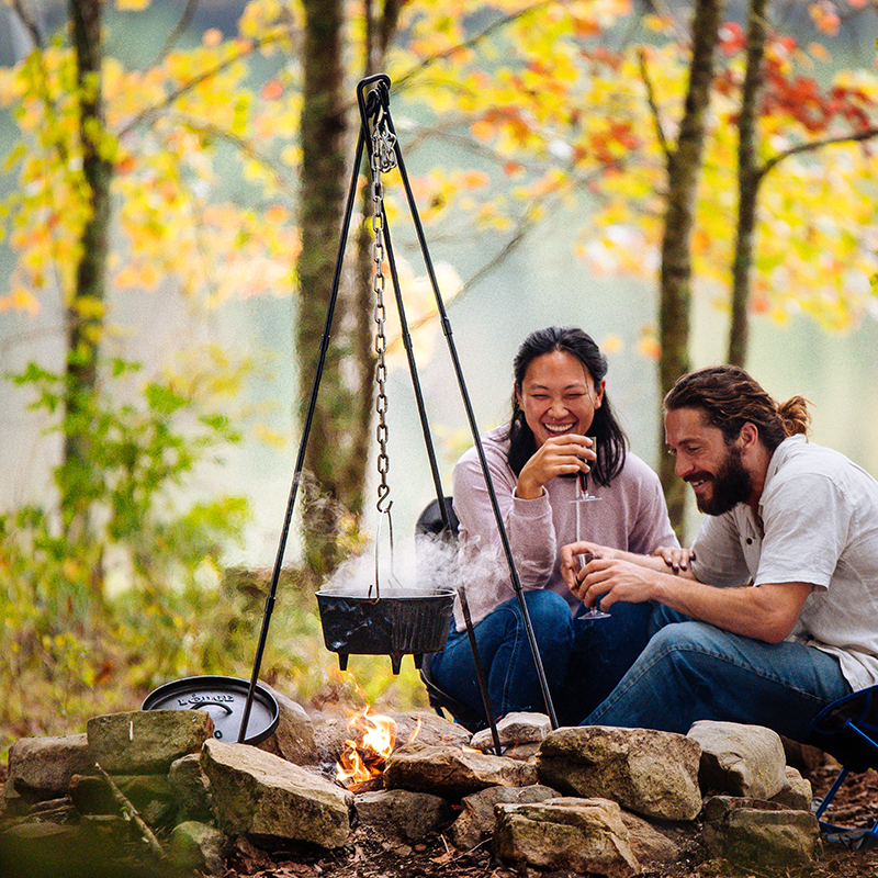A couple having fun near campfire while tripod holds a camp dutch oven.