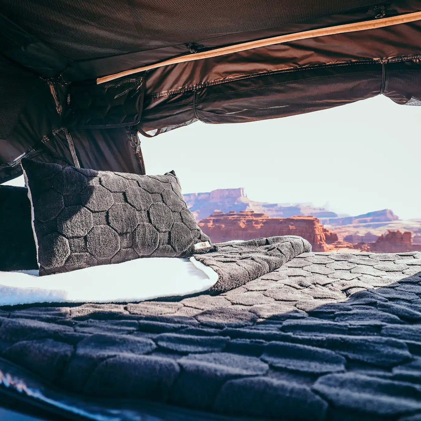 Interior of an FSR Rooftop Tent with Cloud Comforter and pillow cases setup with a scenic desert landscape visible behind the bedding set