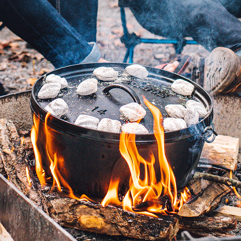 Dutch oven cooking on fire with coals on top.