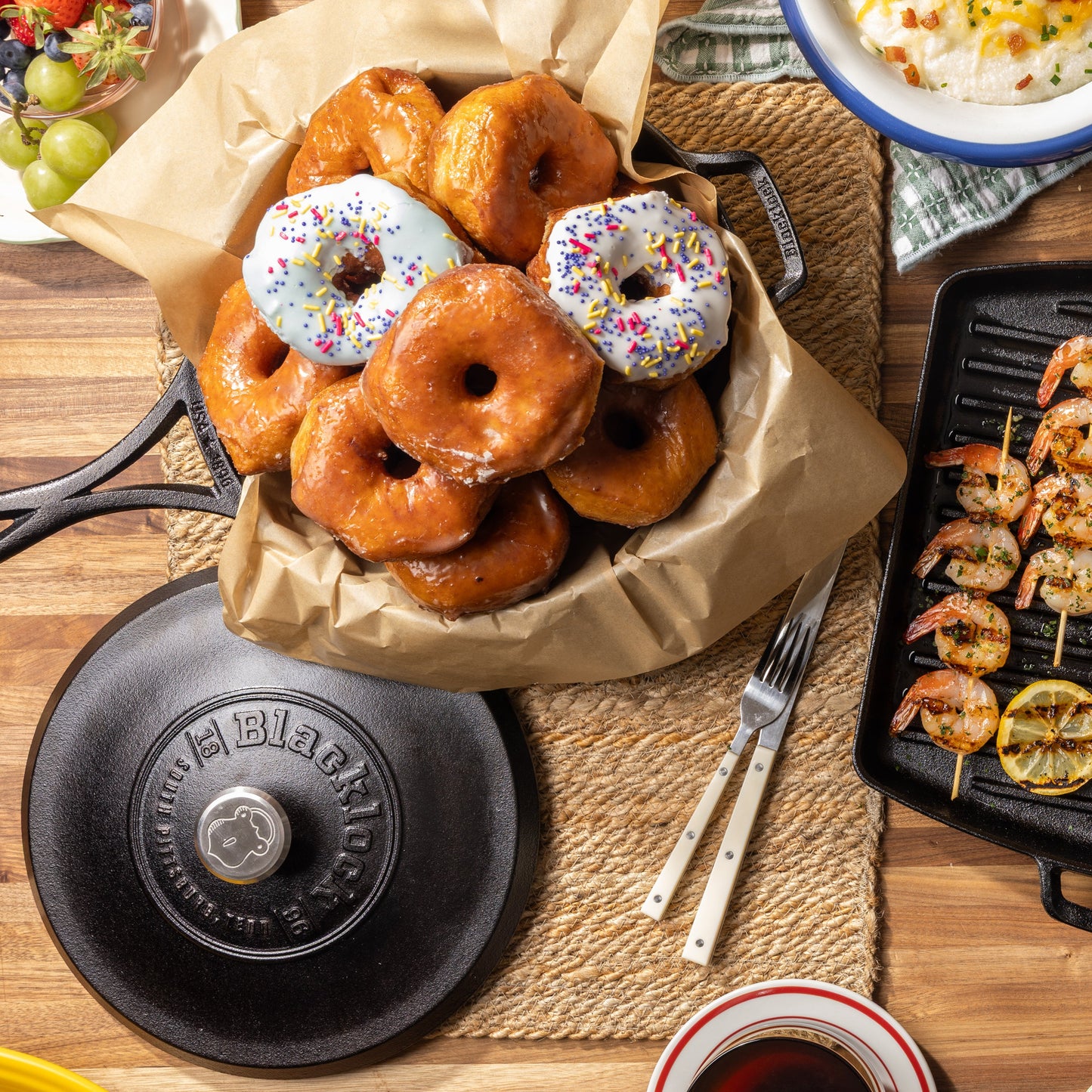 Top view of kitchen table filled with dishes including donuts prepared in skillet.