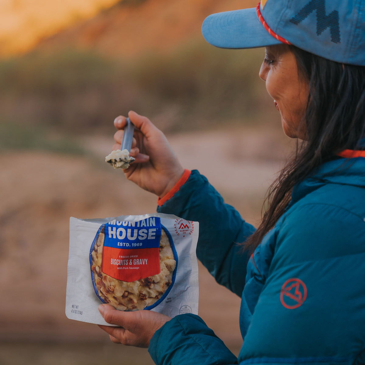 Person smiling as they look at a spoonful of Mountain House Biscuits & Gravy in the backcountry.