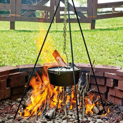 Tripod being used to hold dutch oven over fire in firepit.