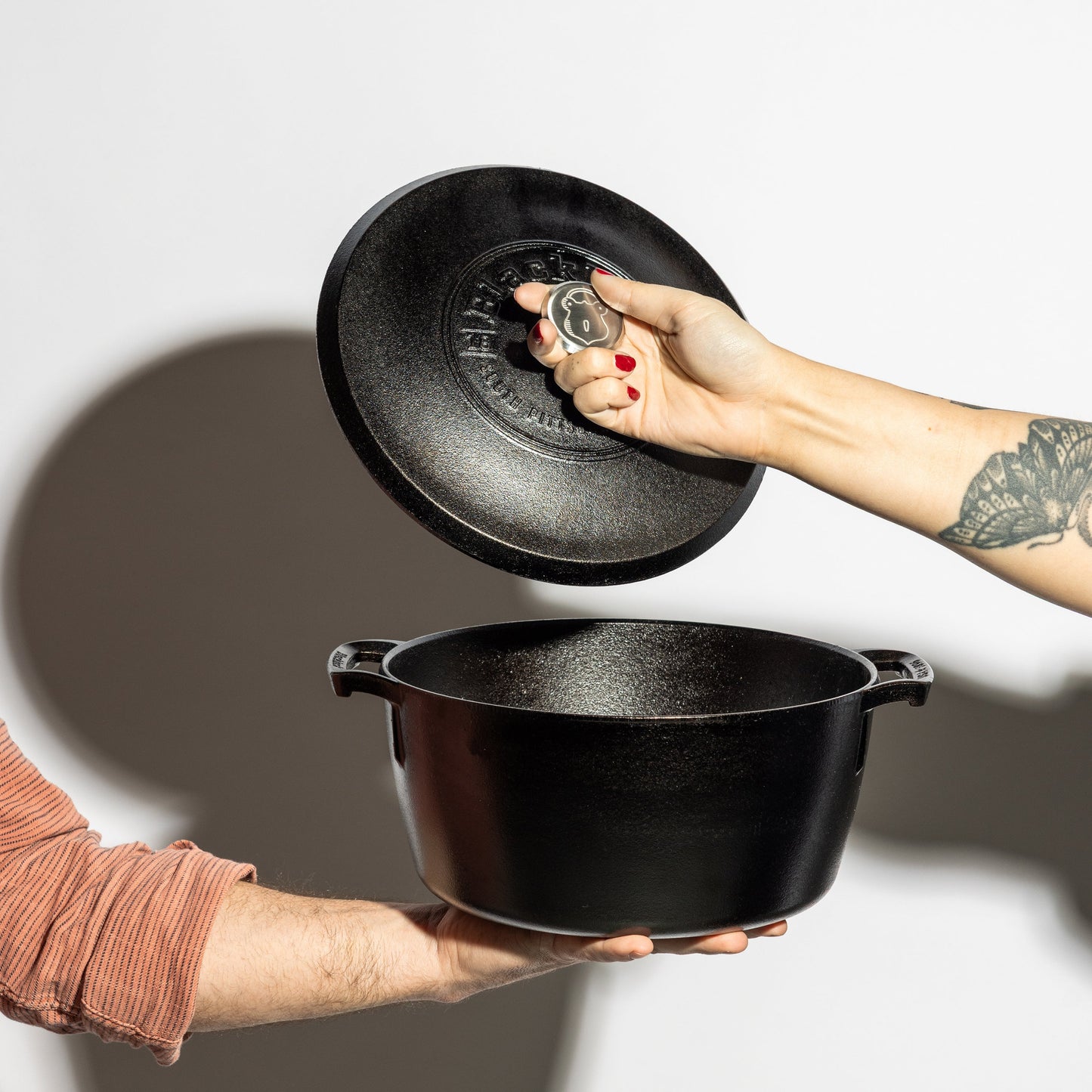 Someone holding dutch oven while someone else lift's the lid.