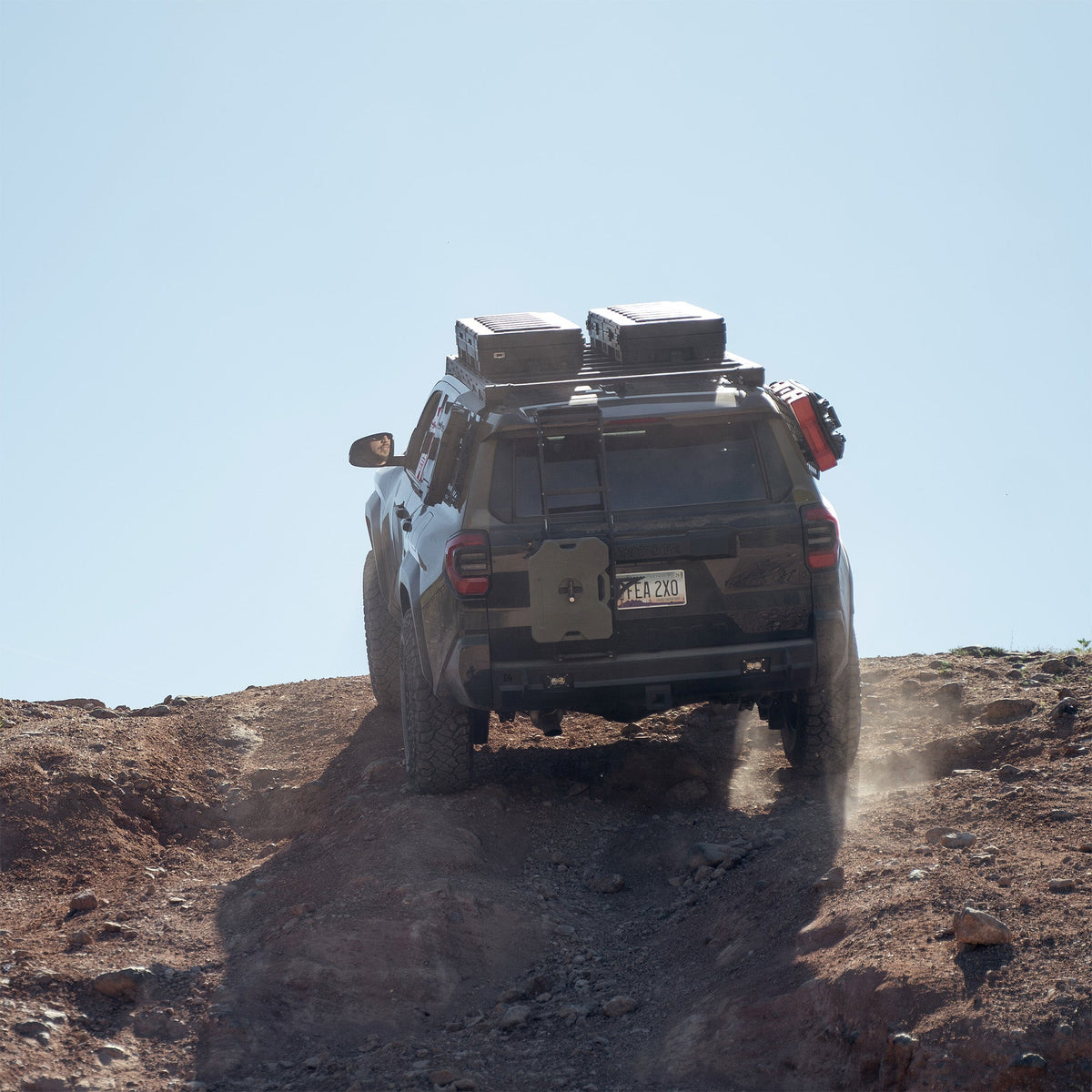 The C4 4Runner build summits a steep rock crawl, equipped with bumpers, roof rack, ladder, and MOLLE panels.