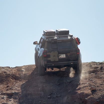 The C4 4Runner build summits a steep rock crawl, equipped with bumpers, roof rack, ladder, and MOLLE panels.