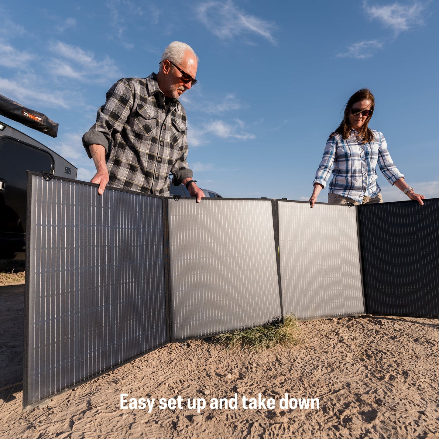 Two people setting up a large solar panel on a sandy ground with a clear blue sky.