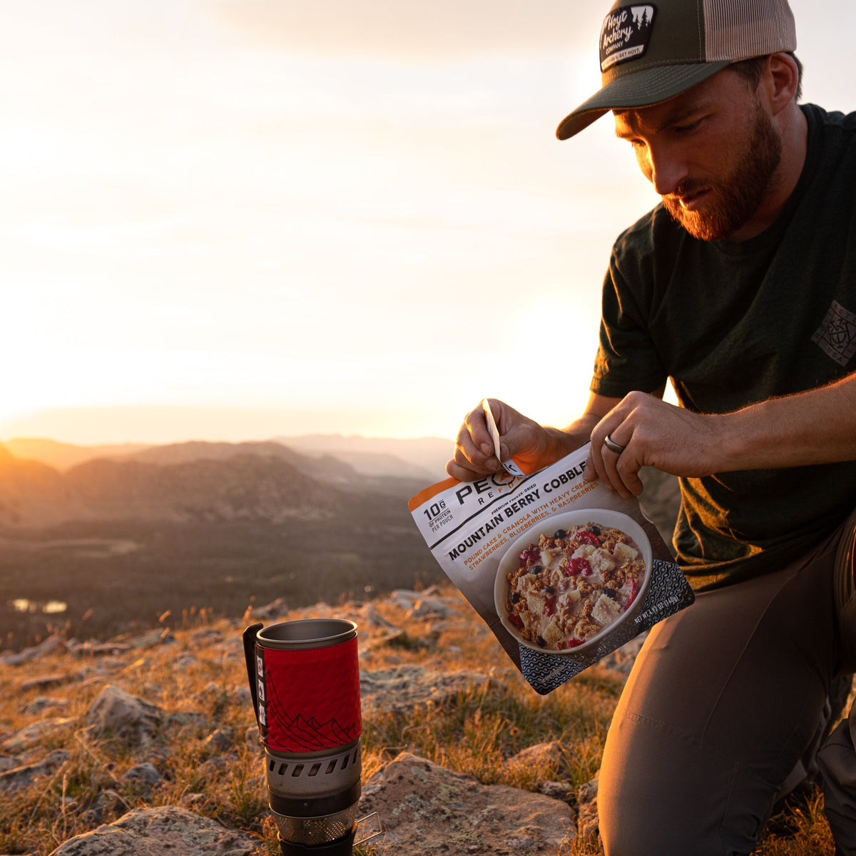 A man kneeling on a rocky hill enjoy a package of Mountain Berry Cobbler dessert.