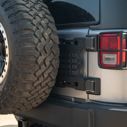 Close-up of a vehicle's rear tire and Jeep Wrangler JK Tailgate Reinforcement Molle Panel on a sunny day.