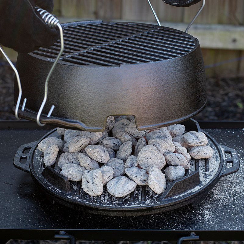 Someone using handles to place top piece over hot coals.
