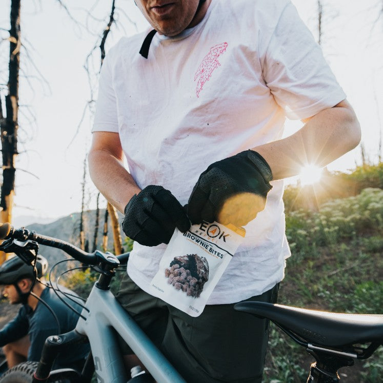 A man wearing gloves holding a bag of brownie bites, a person holding a package of brownie bites, and a man wearing a helmet and gloves holding a package of brownies.