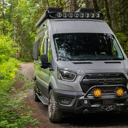 Front view of Ford Transit Van with FVC Transit Side Steps, Safari Roof Rack, and Core Front Bumper installed while driving through the woods