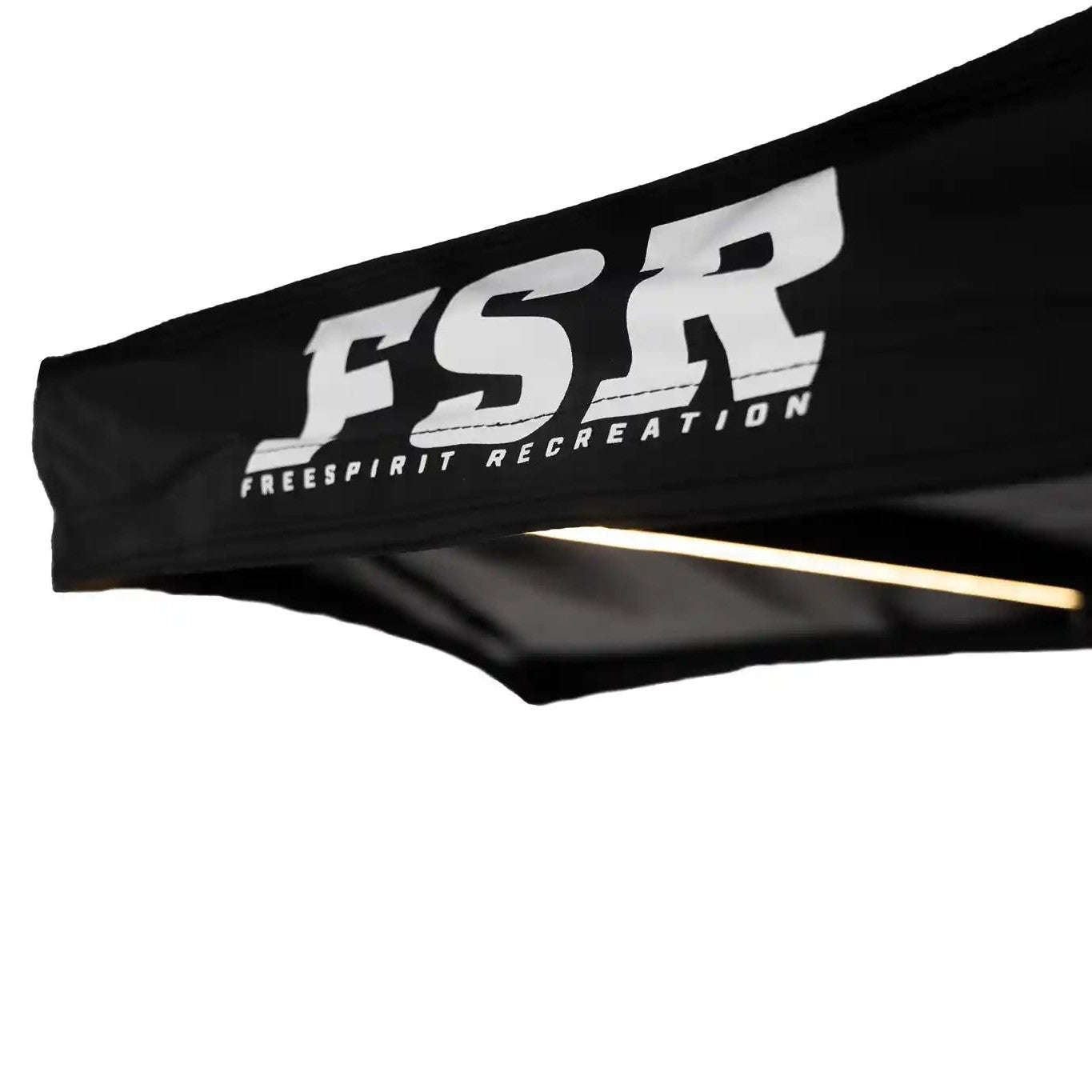 Close-up of the black canopy of the FSR 180 Tailgate Awning with 'FSR Free Spirit Recreation' logo visible and illuminate LED awning light in the background