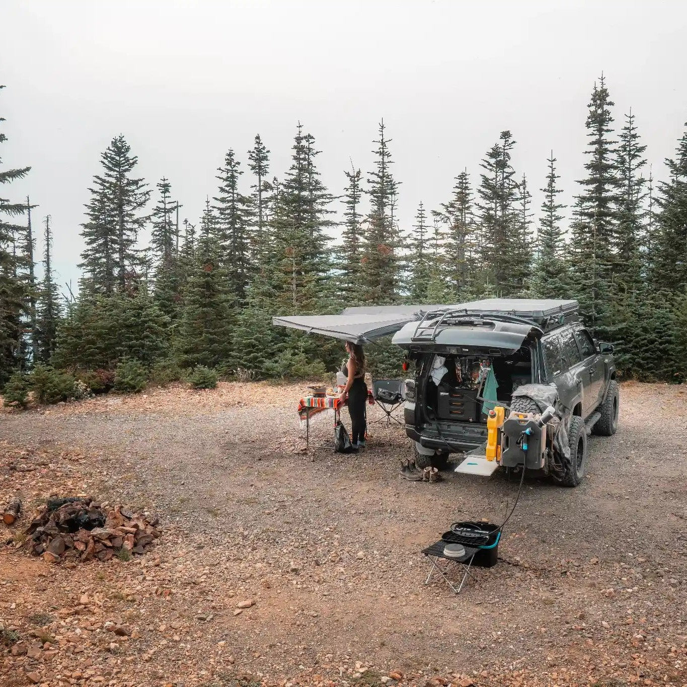 Toyota 4Runner with a FSR 180 degree Awning V2 deployed while camping in a wooded area with table and chairs setup beneath the open awning