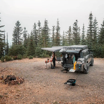 Toyota 4Runner with a FSR 180 degree Awning V2 deployed while camping in a wooded area with table and chairs setup beneath the open awning