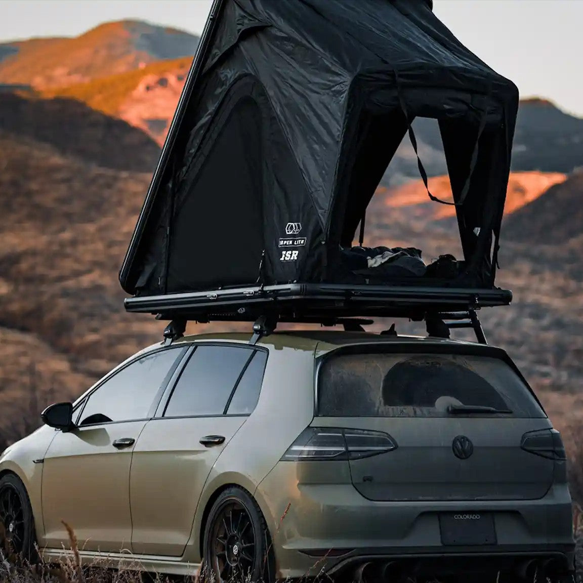 FSR Aspen Lite rooftop tent from Free Spirit Recreation mounted on a compact car and setup in a desert campsite with rmountains in the background