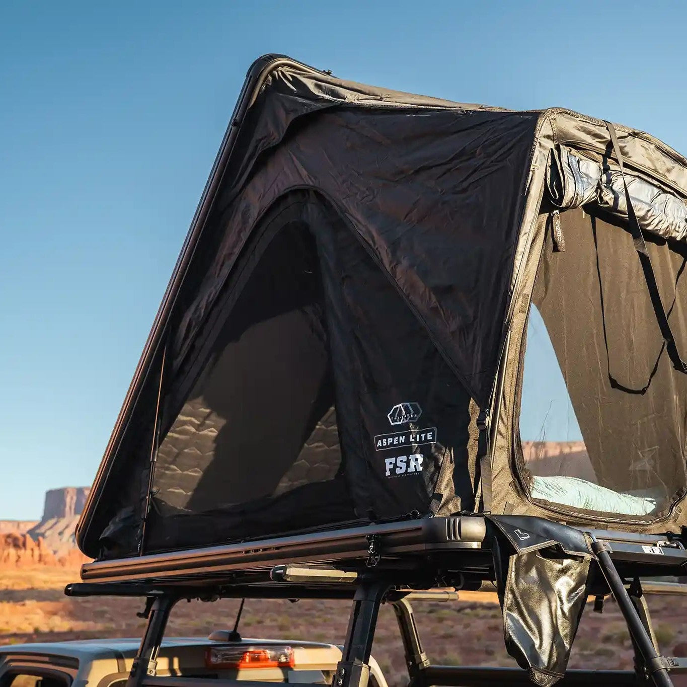Free Spirit Recreation Aspen Lite Standard rooftop tent mounted on a truck bed rack and setup camping in a desert with red rock formations in the background