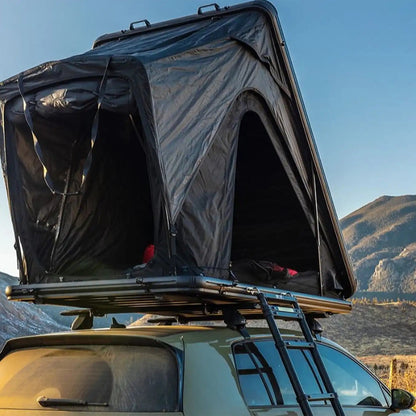 Photo of a person camping in an FSR Aspen Lite Standard Rooftop Tent by Free Spirit Recreation with windows and doors open infront of a mountain range at sunrise