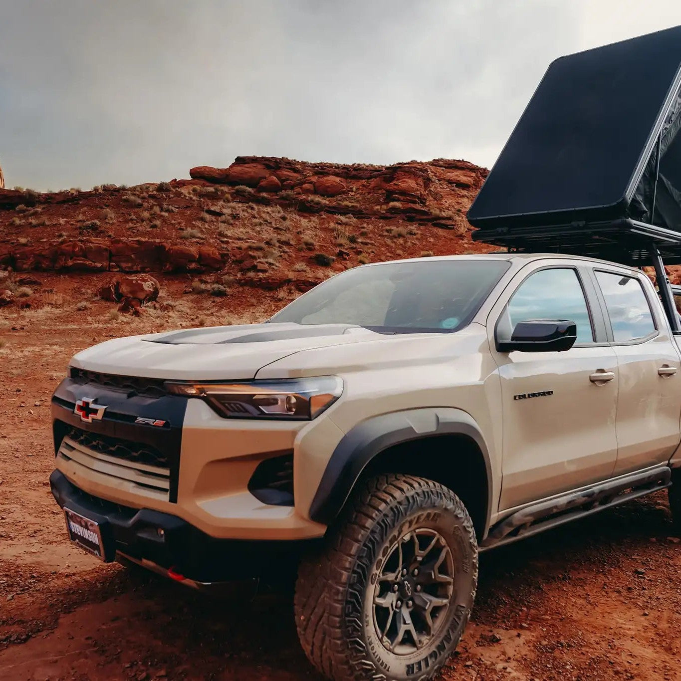 Person camping in an FSR Aspen Lite XL Rooftop Tent mounted on a Chevy Colorado bed rack in the red desert terrain of Moab, Utah