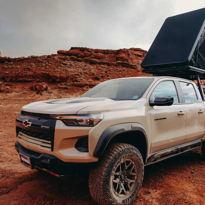 Person camping in an FSR Aspen Lite XL Rooftop Tent mounted on a Chevy Colorado bed rack in the red desert terrain of Moab, Utah