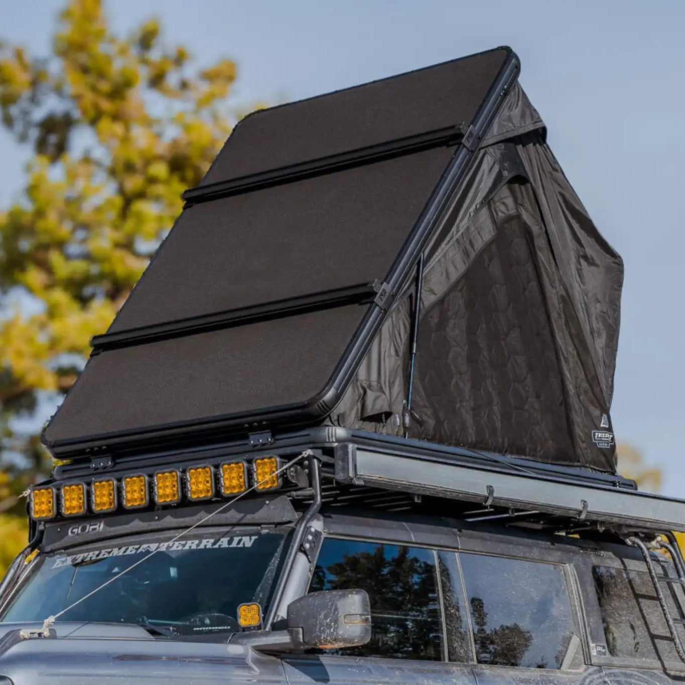 Exterior photo of the FSR Aspen Lite XL Rooftop Tent open and installed on a Ford Bronco while camping in a forested setting
