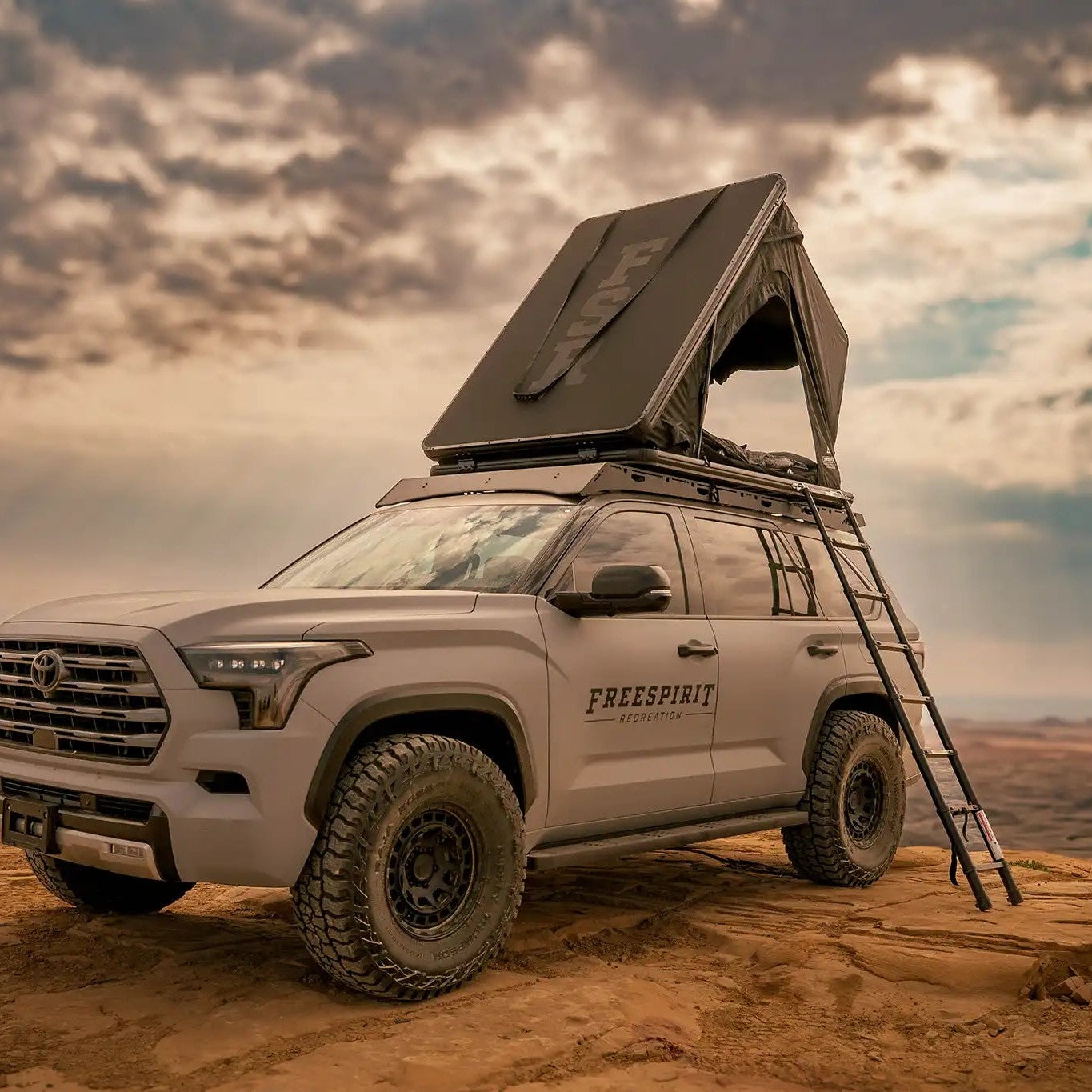 Person camping in an FSR Aspen Lite XL Rooftop Tent with windows and doors open in a desert setting with ladder installed