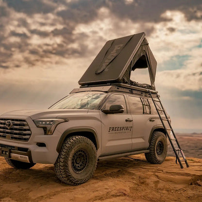 Person camping in an FSR Aspen Lite XL Rooftop Tent with windows and doors open in a desert setting with ladder installed