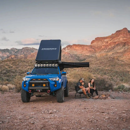 Blue Toyota 4Runner with an FSR Aspen Pro Rooftop Tent setup with Free Spirit Recreation 180 degree awning mounted to the tent and deployed in a desert campsite