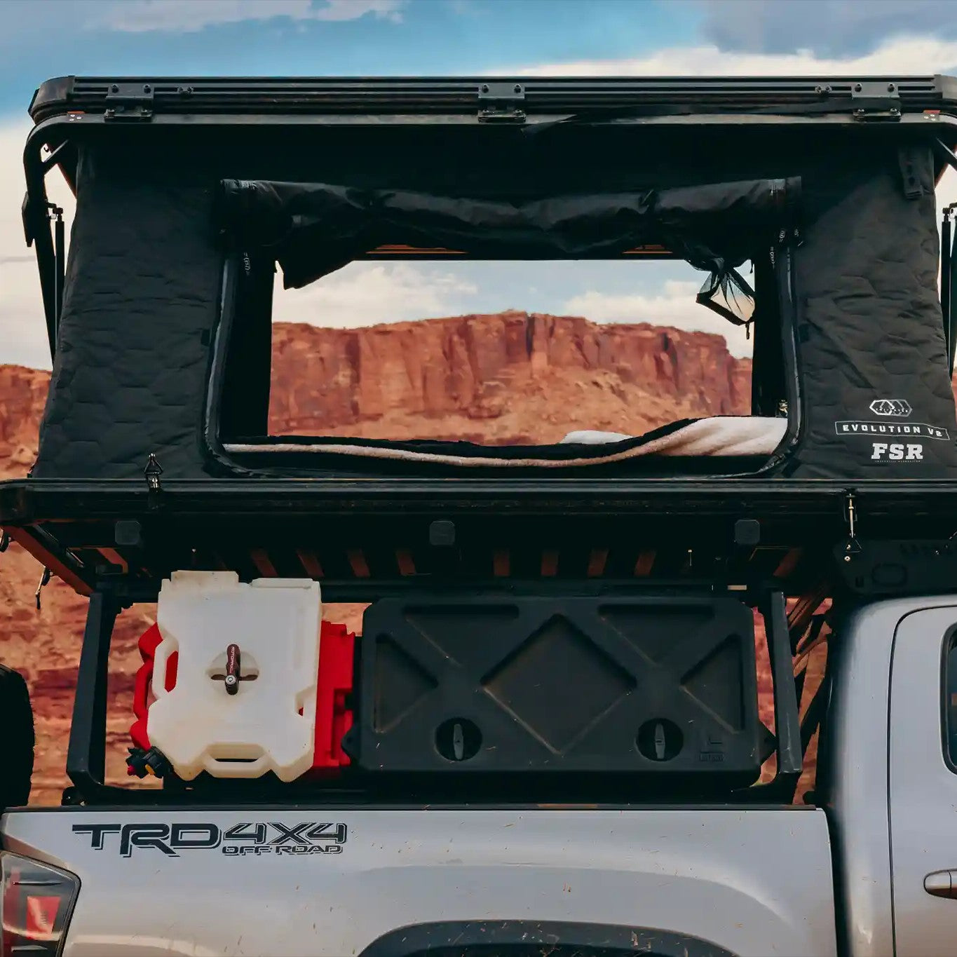 Back of a Toyota Tacoma with an FSR Evo XL rooftop tent mounted on the bed rack and setup for camping against red rock formations in a desert landscape.