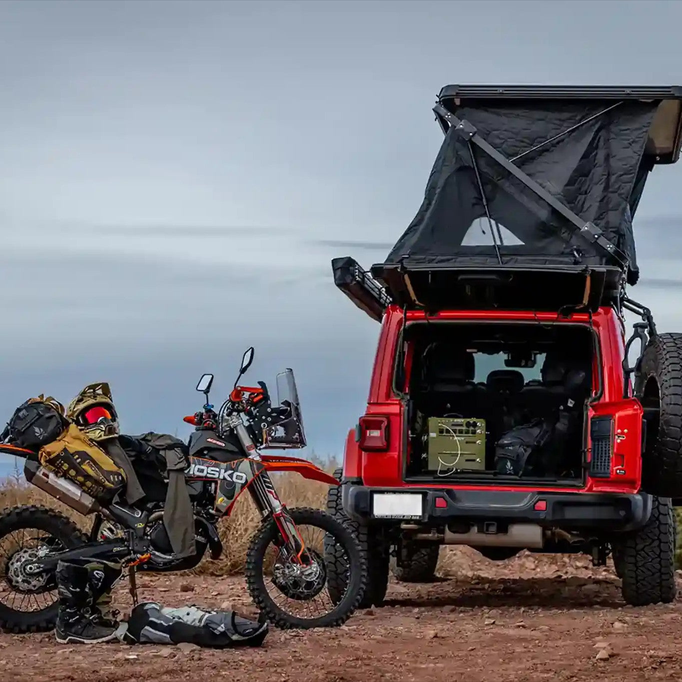 Red Jeep with a FSR Evo XL rooftop tent  setup on top and an enduro motorcycle parked nearby in a desert landscape.
