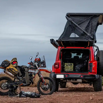 Red Jeep with a FSR Evo XL rooftop tent  setup on top and an enduro motorcycle parked nearby in a desert landscape.