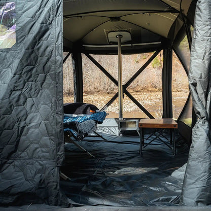 Person camping in the FSR Hub 4 Double Tent, a pop up family camping and glamping tent from Freespirit Recreation with stove installed and roll up walls showing a river in the background