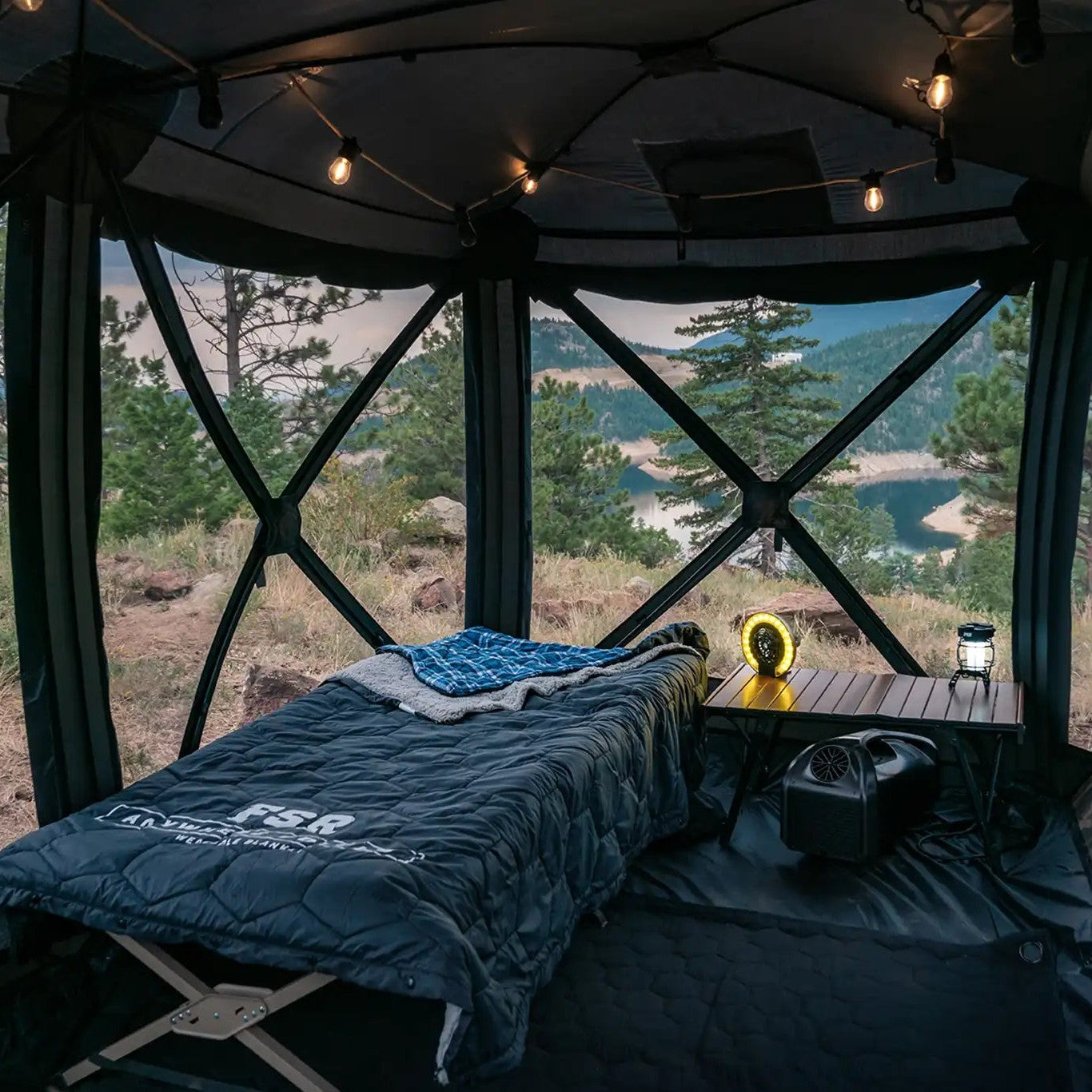 FSR Hub 4 Double Tent, a pop up family camping and glamping tent from Freespirit Recreation setup for camping with interior lights, sleeping cot, table, and all tend walls opened showing the mountainous terrain in the background