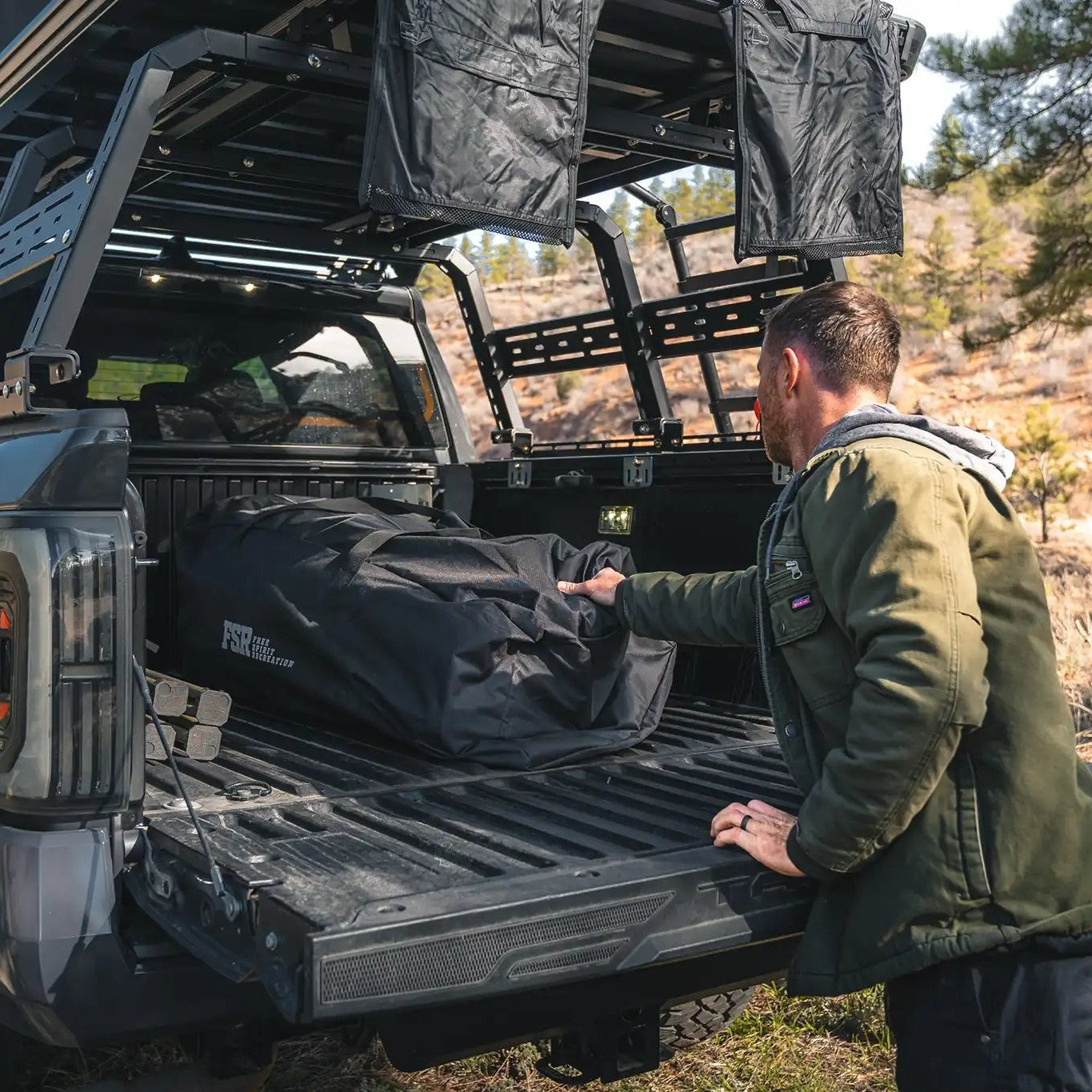 Man removing the FSR Hub 4 Double Tent from Freespirit Recreation, packed in its storage bag, from the back of a truck bed in a wooded campsite.