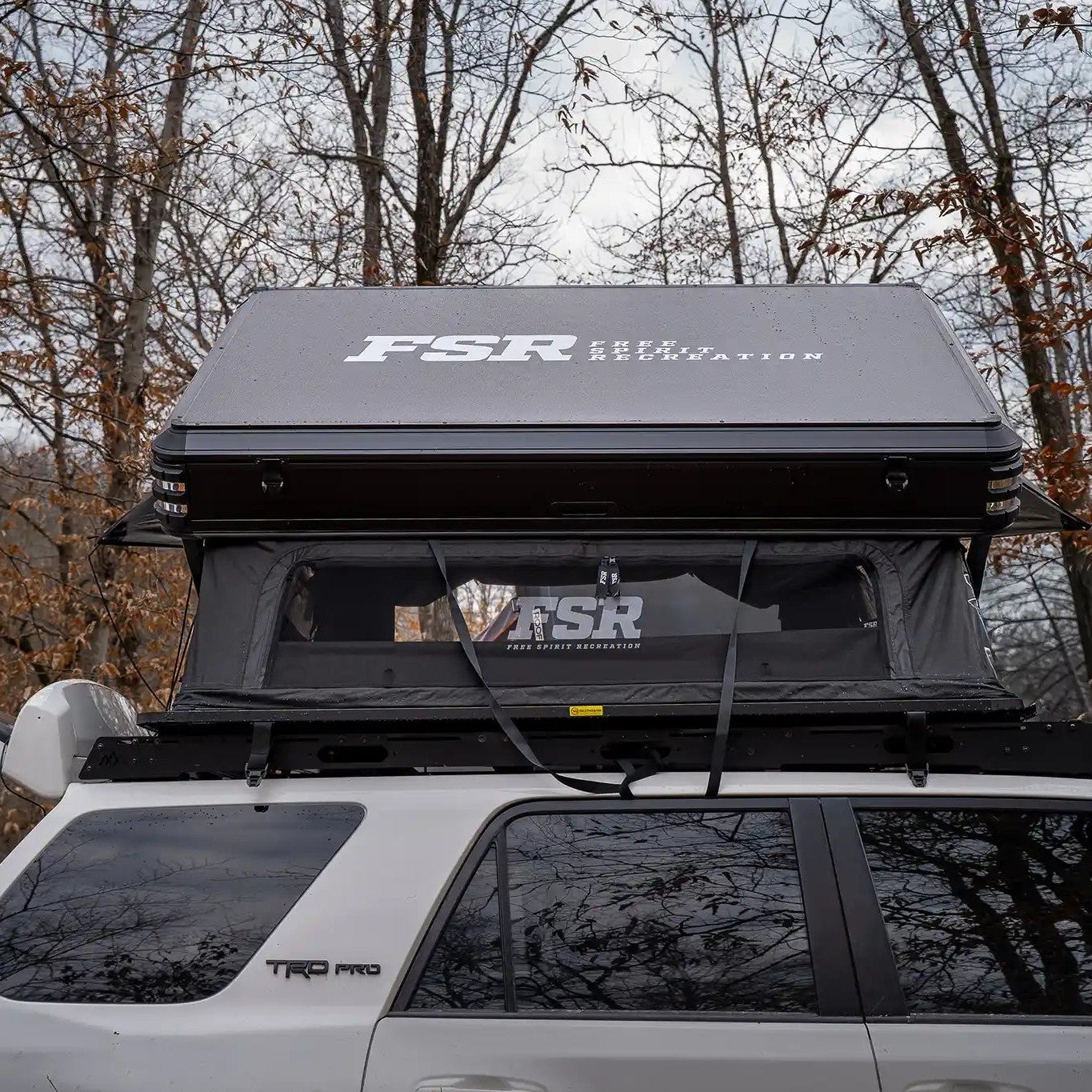 Rear-facing image of the FSR Kali King Rooftop Tent setup while camping in a wooded area with windows open