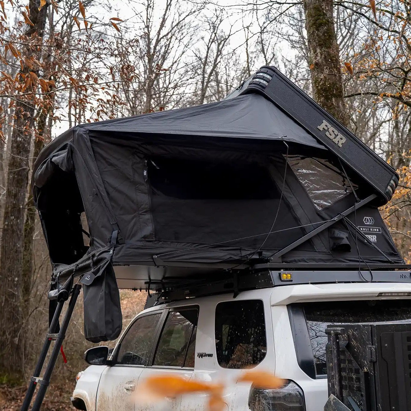 FSR Kali King Rooftop Tent mounted on a white Toyota 4Runner, open and setup for camping in a heavily wooded campsite
