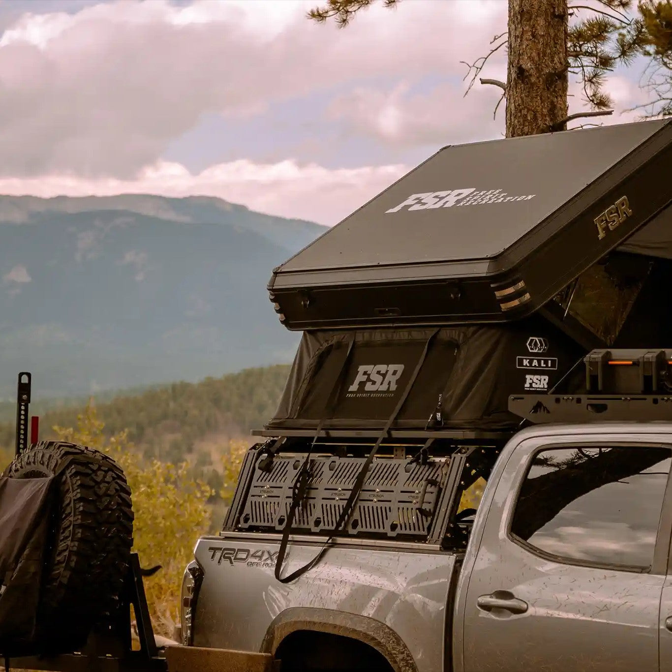 FSR Kali rooftop tent from Free Spirit Recreation mounted and setup on an off road truck in a forested area with mountains in the background
