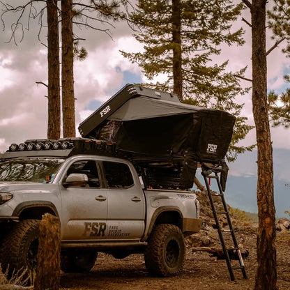 FSR Kali Rooftop Tent from Free Spirit Recreation installed on a Toyota Tacoma bed rack and setup in a wooded campsite with mountains in the background
