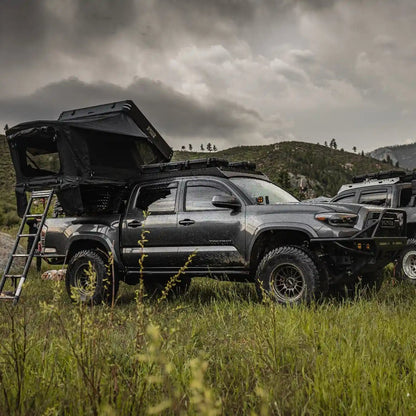 Two Toyota overland trucks with FSR Kali Roof Top Tents setup in a grassy field with mountains in the background