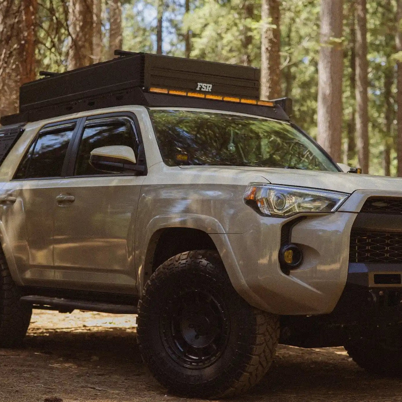 Silver Toyota 4Runner with roof rack and bike on a dirt road in a forest with FSR Nova King Rooftop tent from Free Spirit Recreation on top.
